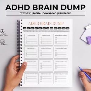 May include: A spiral-bound notebook titled "ADHD Brain Dump" with a layout for organizing tasks, emails, appointments, and more. The notebook is 7" x 9.25" and includes a section for each month of the year. A hand holds a blue pen, ready to write.