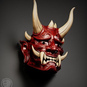 May include: A detailed, red Oni mask with large, off-white horns and fangs. The mask features intricate facial details, including a wide grin and furrowed brow. The mask is set against a dark gray background.