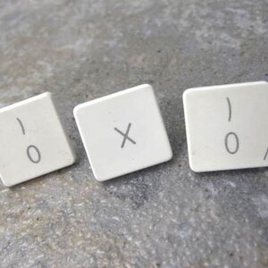 May include: Three white plastic keys with black lettering. The keys are from an Apple computer keyboard. The keys read '0', 'X', and '0'.