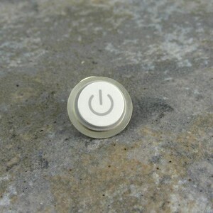 May include: A round, silver-colored push button switch with a white power symbol on it.