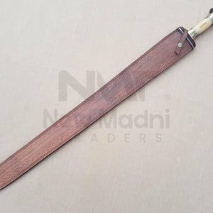May include: A brown leather scabbard with a decorative pattern. The scabbard is for a sword with a brass handle and a black blade.