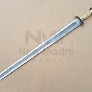 May include: A silver sword with a patterned blade and a bone-colored handle with a brass pommel. The sword is on a brown surface.