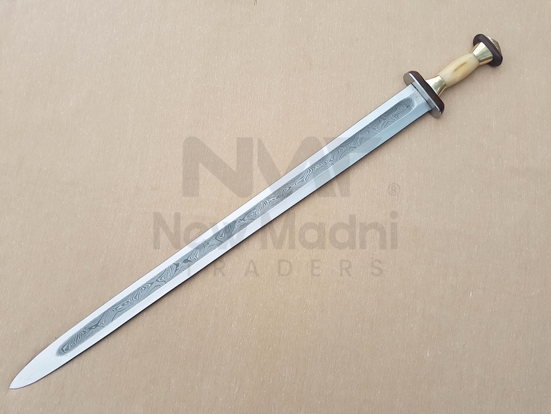 May include: A silver sword with a patterned blade and a bone-colored handle with a brass pommel. The sword is on a brown surface.