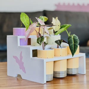 Puede incluir: Un juego de tres tazas de cerámica con un acabado mate moteado. Las tazas son en tonos crema, gris claro y gris oscuro. Cada taza tiene un diseño simple y minimalista y un asa redondeada.