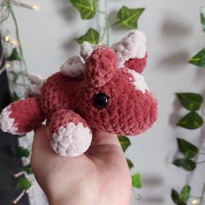 May include: A handcrafted crochet animal toy in red and white. The plush creature features a rounded body, small black eyes, and white detailing on its ears and feet. The soft, textured yarn gives it a cuddly appearance.