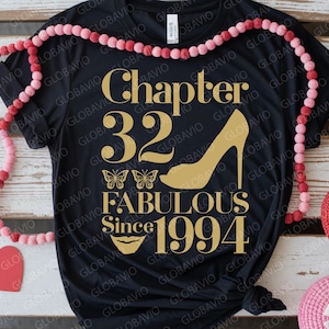 May include: Black t-shirt with gold text that reads "Chapter 32 Fabulous Since 1994." The design includes a high heel, butterflies, and a pair of lips. A pink beaded garland and heart-shaped decorations are in the background.