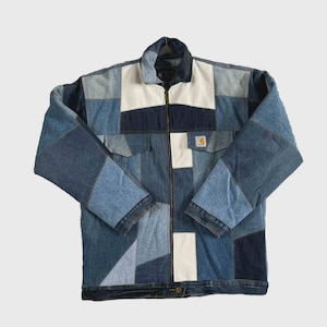 May include: A patchwork denim jacket in shades of blue and white. The jacket features a collared neckline, a full-length zipper, and two chest pockets. The Carhartt logo is visible on the right pocket.