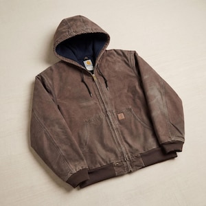 May include: A brown hooded jacket with a full-length zipper, two front pockets, and a brown ribbed hem and cuffs. The jacket has a dark blue lining in the hood. A small square patch is on the right pocket.