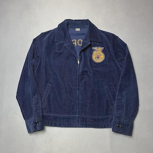 May include: A navy blue corduroy jacket with a zip fastening, two front pockets, and buttoned cuffs. It features a patch with gold and blue embroidery and the text "VOCATIONAL AGRICULTURE". The jacket has a collared neckline.