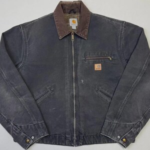 Puede incluir: Chaqueta Carhartt gris oscuro con cuello marr&oacute;n y cremallera completa. La chaqueta tiene dos bolsillos delanteros, un bolsillo en el pecho con cremallera y un peque&ntilde;o parche con el logotipo. La chaqueta est&aacute; hecha de un material duradero y desgastado.