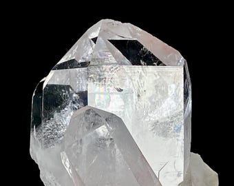 May include: A clear, multi-faceted quartz crystal cluster featuring sharp, pointed terminations and internal fractures that create subtle rainbow light refractions. The mineral specimen displays a transparent, glass-like texture with geometric faces.
