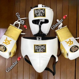Puede incluir: Casco de boxeo blanco, protector de ingle y guantes con detalles dorados. El casco y el protector de ingle tienen el texto "No Boxing No Life" impreso. Los guantes tienen el texto "No Boxing No Life" impreso en el lateral.