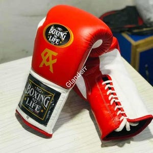 K&ouml;nnte beinhalten: Ein Paar rote und wei&szlig;e Boxhandschuhe mit wei&szlig;en Schn&uuml;rsenkeln. Die Handschuhe haben einen schwarzen Aufn&auml;her mit dem Text "NO BOXING NO LIFE" in wei&szlig;en Buchstaben.