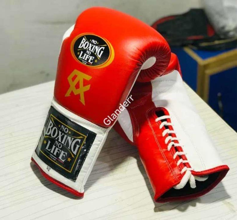 K&ouml;nnte beinhalten: Ein Paar rote und wei&szlig;e Boxhandschuhe mit wei&szlig;en Schn&uuml;rsenkeln. Die Handschuhe haben einen schwarzen Aufn&auml;her mit dem Text "NO BOXING NO LIFE" in wei&szlig;en Buchstaben.