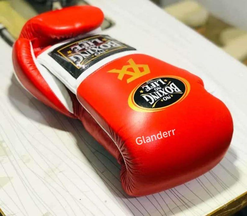 K&ouml;nnte beinhalten: Rote Boxhandschuhe mit wei&szlig;em Besatz und dem Text "No Life No Boxing" in einem goldenen Kreis. Die Handschuhe haben ein wei&szlig;es Logo mit einem schwarzen "X" und dem Text "Glanderr" in wei&szlig;.