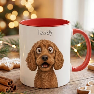 Könnte beinhalten: Ein weißer Keramikbecher mit rotem Innenraum und rotem Henkel, der eine Cartoon-Illustration eines braunen Hundes mit lockigem Fell zeigt, wobei der Name Teddy in schwarzer Schrift über dem Kopf des Hundes auf der Vorderseite steht.