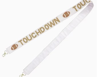 May include: White shoulder strap with gold-colored text and football graphics that read "TOUCHDOWN." The strap has gold-colored metal clasps on each end. The strap is designed for a bag or purse.