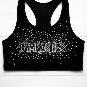 May include: Black sports bra with the word "GYMNASTICS" spelled out in sparkling rhinestones. The bra has a racerback design and is covered in small, glittering rhinestones.