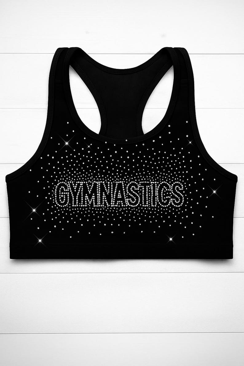 May include: Black sports bra with the word "GYMNASTICS" spelled out in sparkling rhinestones. The bra has a racerback design and is covered in small, glittering rhinestones.