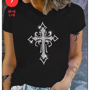 May include: Black V-neck t-shirt featuring a sparkling, rhinestone-studded cross design. The cross is the focal point, with intricate detailing. The shirt has a classic fit and short sleeves. The image also shows the text "W=6 L=8" and the number "7".