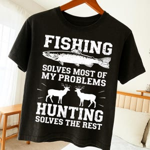 Può includere: T-shirt nera con testo e grafica bianchi. Il testo in alto recita "FISHING" sopra un'illustrazione di pesce. Sotto il pesce, il testo recita "SOLVES MOST OF MY PROBLEMS". Il testo in basso recita "HUNTING SOLVES THE REST" con illustrazioni di cervi.