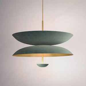 May include: A contemporary pendant light. It has two large, teal-coloured, saucer-shaped shades, with a gold-coloured interior on the lower shade. A smaller teal shade hangs below. The fixture is suspended by a gold-coloured rod, creating a layered design.