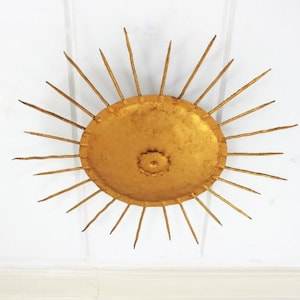 Puede incluir: Una decoración de pared de sol de metal dorado con un centro redondo y puntos radiantes.