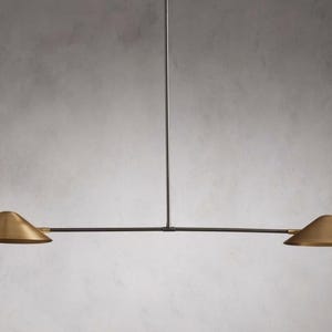 Puede incluir: Una lámpara colgante moderna de dos luces con un marco de metal negro y dos pantallas de color latón.