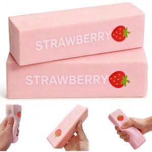 Può includere: Due blocchi rettangolari rosa chiaro e comprimibili che presentano la parola STRAWBERRY in lettere maiuscole bianche e una piccola grafica di fragola rossa con una foglia verde. I blocchi sono realizzati in un materiale morbido e flessibile comprimibile a mano.