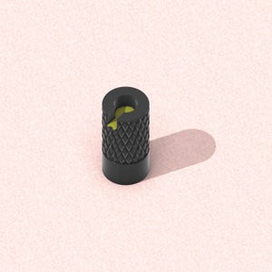 以下が含まれることがあります： 下部にひし形模様、上部に円形部分がある黒い円筒形の物体。内部は黄色です。物体はピンク色の表面に影を落としています。