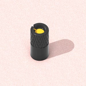 以下が含まれることがあります： 上部にダイヤモンド模様、内部に黄色のインサートが付いた黒いタイヤバルブステムキャップ。 キャップは円筒形で、ピンク色のテクスチャ加工された表面に置かれ、影を落としています。