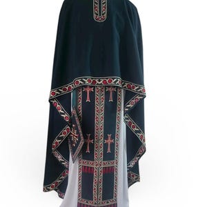 May include: A dark green liturgical vestment with ornate red and gold embroidery. The vestment features a cape, a stole with crosses, and a matching pouch. The design includes intricate patterns and tassels, set against a white undergarment.