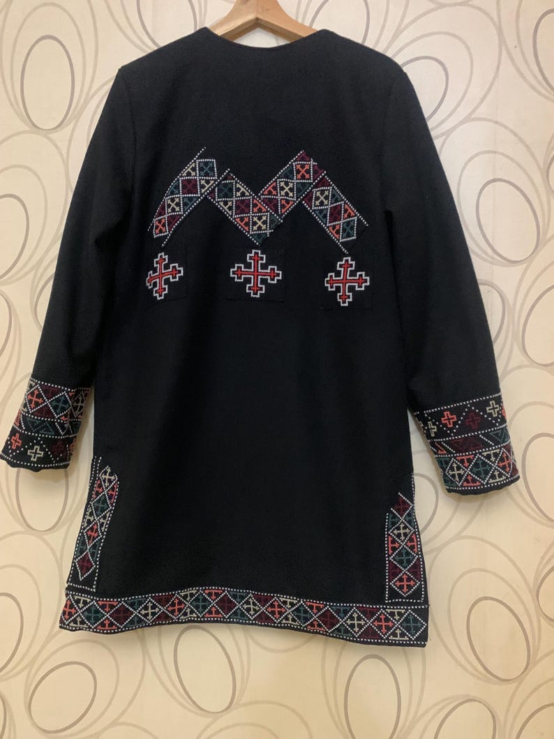 Puede incluir: Chaqueta negra de manga larga con coloridos patrones geom&eacute;tricos bordados en la espalda y las mangas. El bordado presenta un patr&oacute;n repetitivo de cruces y diamantes.