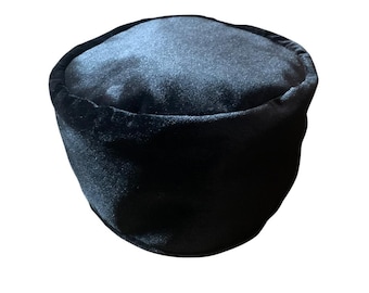 May include: A black velvet hat with a rounded top and a cylindrical shape. The hat has a soft, plush texture and a dark, solid color. The hat is a traditional style.