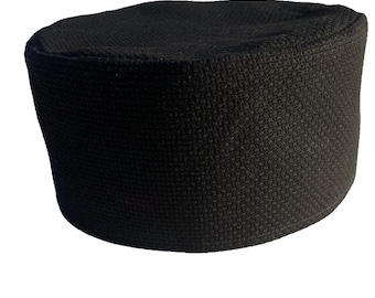 Puede incluir: Un gorro kufi negro con una apariencia tejida y texturizada. El gorro tiene forma cilíndrica con la parte superior plana y está hecho de un material oscuro de color sólido. Este tocado tradicional es adecuado para diversas ocasiones.