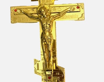 Może przedstawiać: Złoty krzyż prawosławny z szczegółowym przedstawieniem Jezusa Chrystusa. Krzyż posiada skomplikowane rzeźbienia, czerwone akcenty i aureolę wokół głowy Chrystusa. Projekt zawiera ikonografię religijną i tekst.