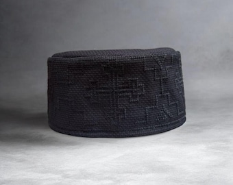 Puede incluir: Un gorro cilíndrico negro con una textura tejida estructurada y un patrón geométrico de cruces repetido en toda la superficie. La prenda para la cabeza tiene una parte superior plana y una banda firme y erguida de forma circular.