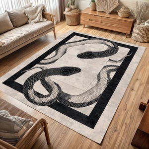 May include: A rectangular rug with a black and white snake design. The snakes are intertwined within a black border, set against a neutral background. The rug is placed on a wooden floor in a living room setting.