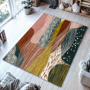 Peut inclure: Un tapis rectangulaire avec un motif abstrait. Il présente un mélange de couleurs : marron, rose, vert et jaune. Des lignes blanches et des motifs pointillés créent de la texture. Le tapis est posé sur un plancher en bois clair.