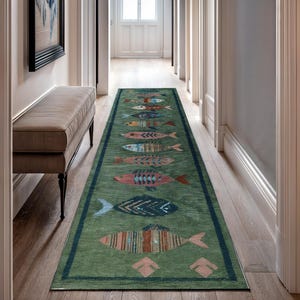 Könnte beinhalten: Ein langer, rechteckiger grüner Teppich mit einem dunkelblauen Rand. Der Teppich zeigt ein sich wiederholendes Muster aus bunten Fischen in verschiedenen Designs. Die Fische sind in den Farbtönen Rosa, Blau, Orange und Braun gehalten. Der Teppich liegt in einem Flur.