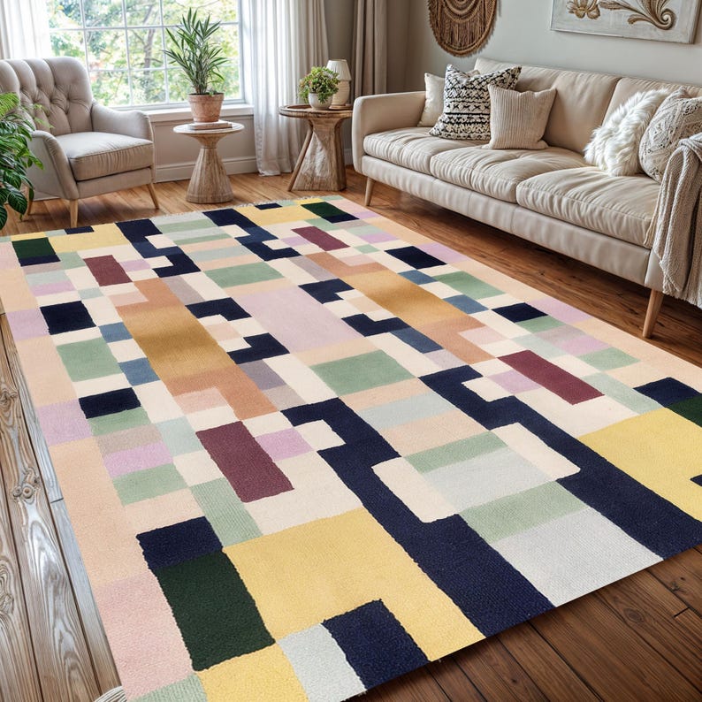 May include: A rectangular area rug with a geometric pattern in various colors. The rug features blocks of yellow, navy, green, pink, and beige. The rug is placed on a hardwood floor in a living room setting.