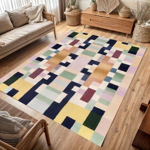 May include: A rectangular area rug with a geometric pattern in a variety of colors, including yellow, navy, green, and purple. The rug is placed on a hardwood floor in a living room setting. The design features a block-like pattern.