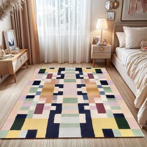 May include: A rectangular area rug with a geometric pattern in various colors, including yellow, navy, green, purple, and beige. The rug is placed on a hardwood floor in a bedroom setting.