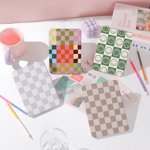 May include: Four different patterned covers for an e-reader. The covers are in a variety of colors and patterns, including a blue and white checkered pattern, a brown and white checkered pattern, a green pattern with smiley faces, and a multi-colored checkered pattern.