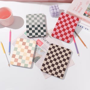 May include: Four different checkerboard patterned Kindle e-reader cases. The cases are green and black, red and pink, beige and black, and light green and beige.