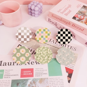 May include: Six different patterned coasters, including checkered, floral, and geometric designs. The coasters are on a newspaper and a pink surface.