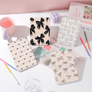May include: Four different e-reader covers with a pink background. The covers feature various bow designs in black and white on a light pink background.
