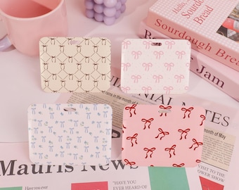 May include: Four different patterned name tag holders. The holders are made of a white plastic material and have a hole at the top for a lanyard. The patterns are: a brown and white bow pattern, a pink and white polka dot pattern with bows, a blue and white bow pattern, and a pink pattern with red bows.