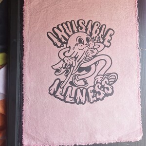 May include: Pink fabric patch with a black and white illustration of a cartoon ghost with the text "Invisible Illness".