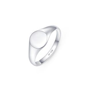 May include: A polished silver signet ring with a smooth, circular face. The ring has a rounded band and a simple, elegant design. The metal is stamped with "am 925".